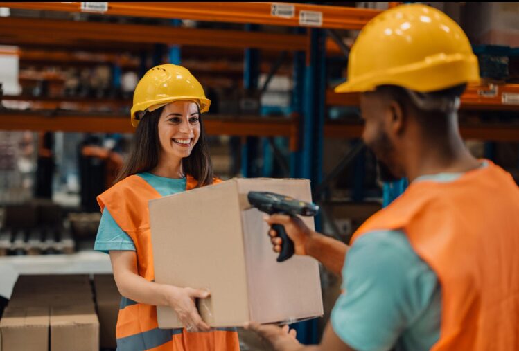 2 warehouse workers, 1 is holding a box and the other is scanning the box