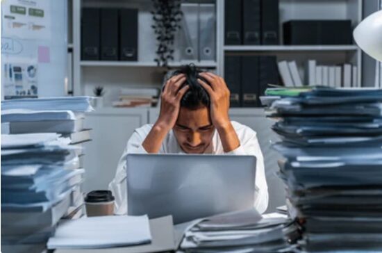 person stressing in front of laptop with piles of paper